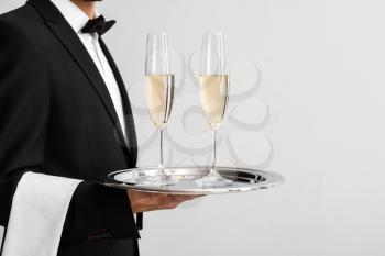 Waiter with glasses of champagne on light background�