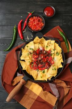 Frying pan with tasty nachos, minced meat and chili on wooden table�