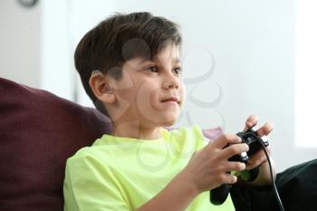 Little boy with hearing aid playing video game at home�