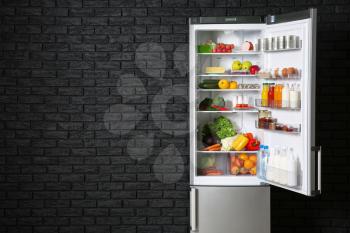 Open fridge full of food near dark brick wall�