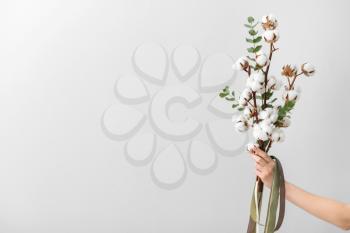 Female hand holding floral composition with cotton flowers on light background�