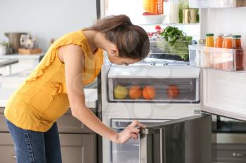 Pregnant woman taking food out of fridge at home�