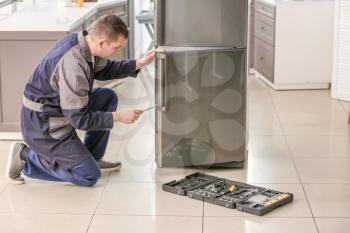 Male technician repairing refrigerator in kitchen�