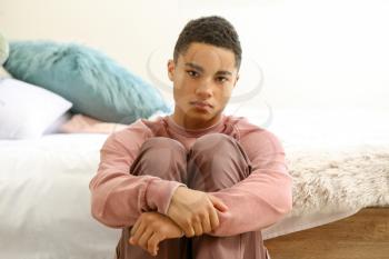 Sad African-American teenage boy sitting in bedroom�