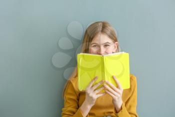 Portrait of cute teenage girl with book on color background�