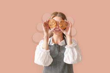 Happy female baker with tasty cookies on color background�