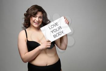 Plus size woman holding paper with text LOVE YOUR BODY on grey background. Concept of body positive�