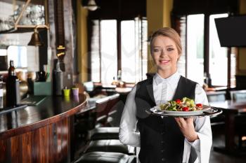 Young female waiter with salad in restaurant�