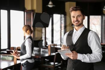 Young male waiter with notebook in restaurant�