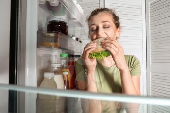 Beautiful young woman eating food near fridge, view from inside�
