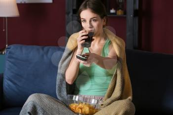 Beautiful young woman eating unhealthy food while watching TV at night�