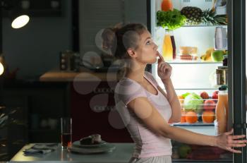 Beautiful young woman looking into fridge at night�