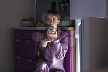 Afraid woman caught in the act of eating tasty unhealthy food near refrigerator at night�