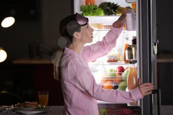 Beautiful young woman choosing food in refrigerator at night�