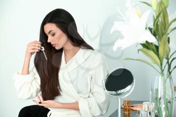 Beautiful young woman applying serum onto her healthy long hair at home�