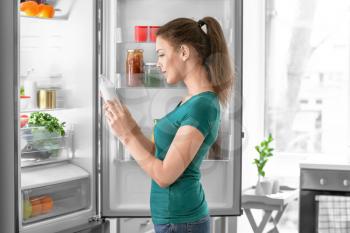Woman taking food out of fridge at home�