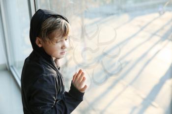 Homeless little boy near window indoors�