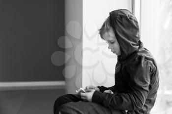 Homeless little boy with bread sitting on window sill indoors�