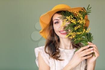 Beautiful young woman with bouquet of mimosa flowers on color background�