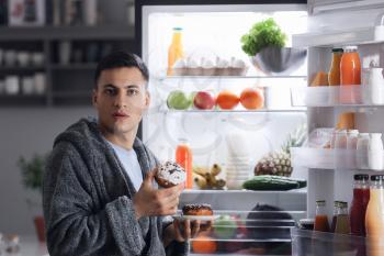 Afraid man caught in the act of eating unhealthy food near refrigerator at night�