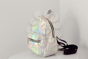 Stylish backpack from iridescent material on table near white wall�