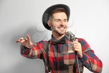 Handsome male singer with microphone on light background�