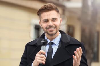 Handsome reporter with microphone outdoors�