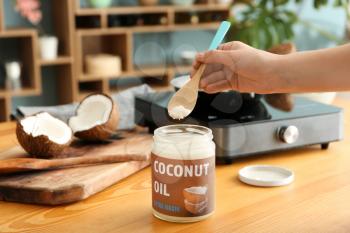 Woman cooking with coconut oil in kitchen�