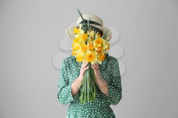 Woman with bouquet of beautiful daffodils on light background�