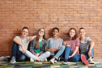 Group of teenagers sitting on floor near brick wall�