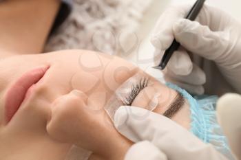 Young woman undergoing procedure of eyelashes lamination in beauty salon�
