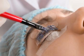 Young woman undergoing procedure of eyelashes dyeing and lamination in beauty salon, closeup�