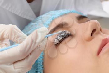 Young woman undergoing procedure of eyelashes dyeing and lamination in beauty salon�
