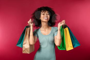 Happy African-American woman with shopping bags on color background�