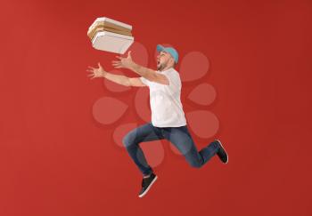 Jumping male courier with pizza boxes on color background�
