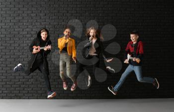 Jumping band of teenage musicians against dark wall�