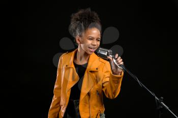 African-American girl with microphone singing against dark background�