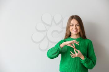 Young deaf mute woman using sign language on light background�