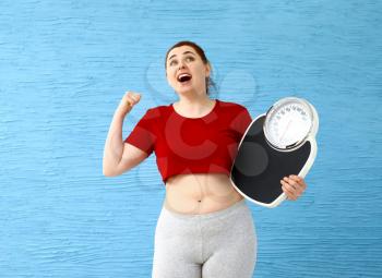 Happy overweight woman with scales on color background. Weight loss concept�