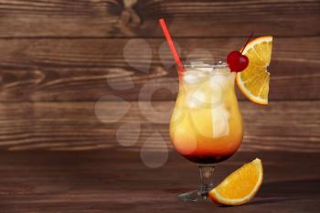Glass of tasty Tequila Sunrise cocktail on wooden background�