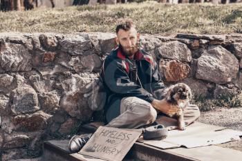 Poor homeless man with dog sitting on stairs outdoors�