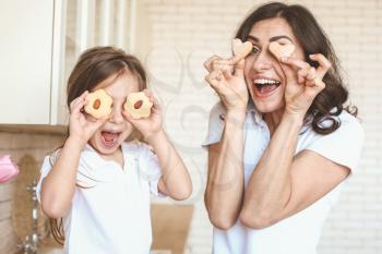 Happy mother and daughter with tasty cookies having fun in kitchen at home�