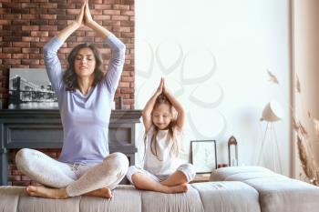 Mother with little daughter meditating at home�