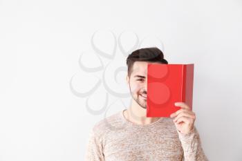 Handsome young man with book on light background�