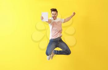 Jumping young man with book on color background�