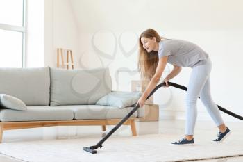 Young woman hoovering carpet at home�