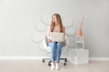 Beautiful young woman with laptop sitting on chair indoors�