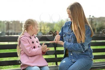 Mother teaching her deaf mute daughter to use sign language outdoors�