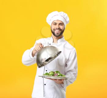 Handsome male chef with salad on color background�