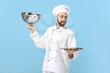 Handsome male chef with empty tray on color background�